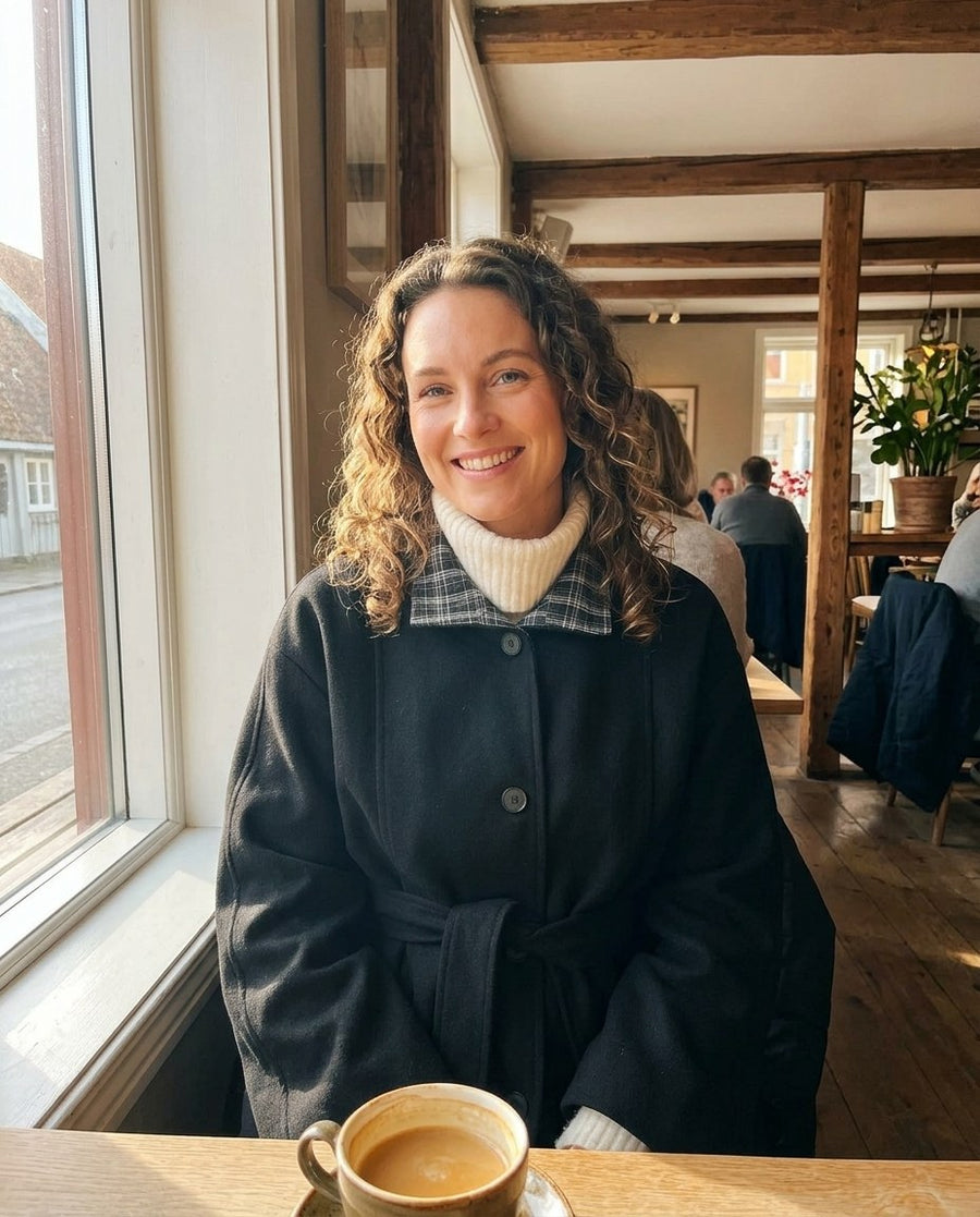 Greta, kappa med skärp och kontrastkrage för dam i svart, stylinginspiration på ett kafé