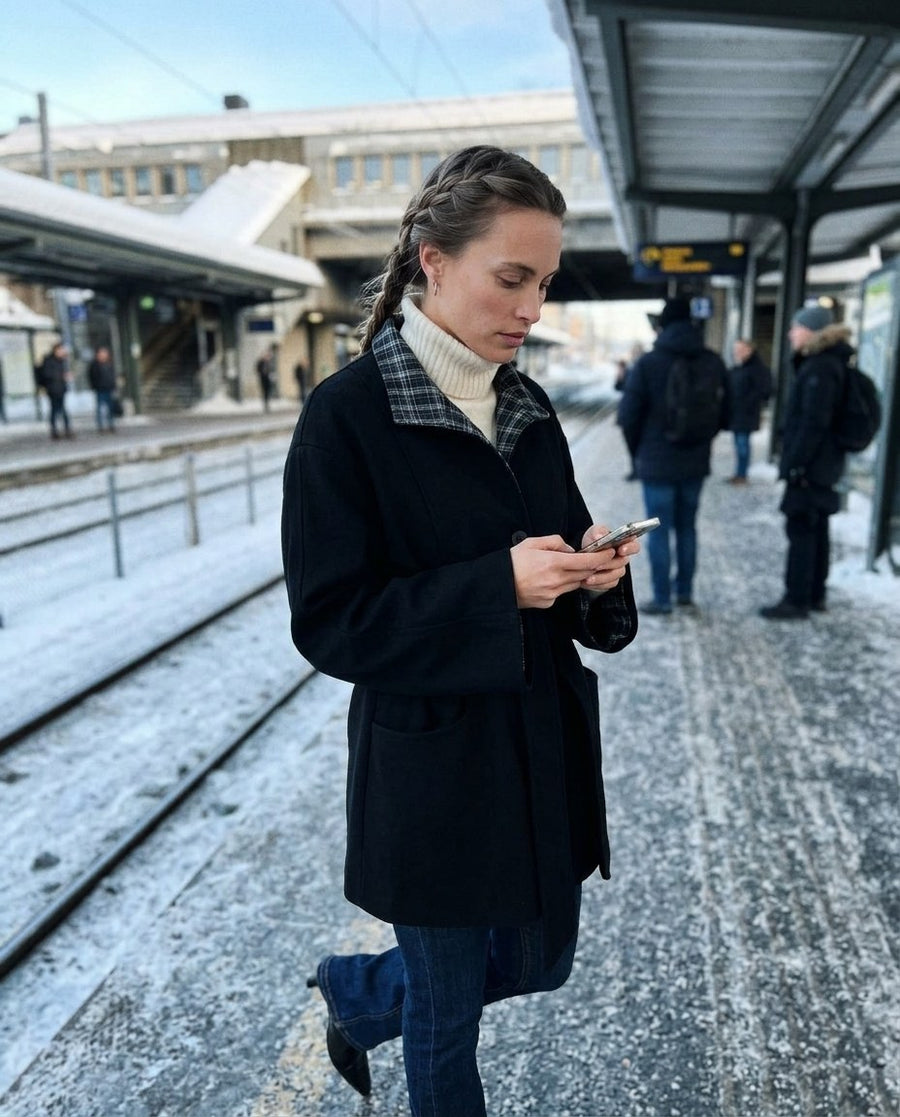 Greta, kappa med skärp och kontrastkrage för dam i svart, stylinginspiration på en perron