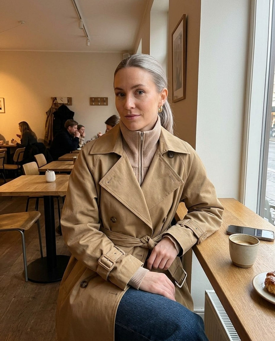 Elin, kort trenchcoat med skärp för dam i beige, stylinginspiration på ett kafé