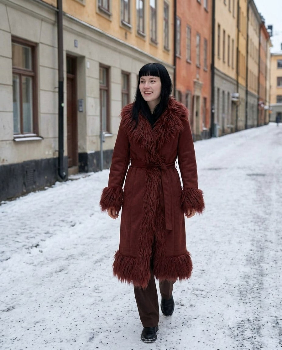Lova, lång kappa i mockaimitation med fuskpälskant för dam i rödbrun, stylinginspiration på en snöig gata