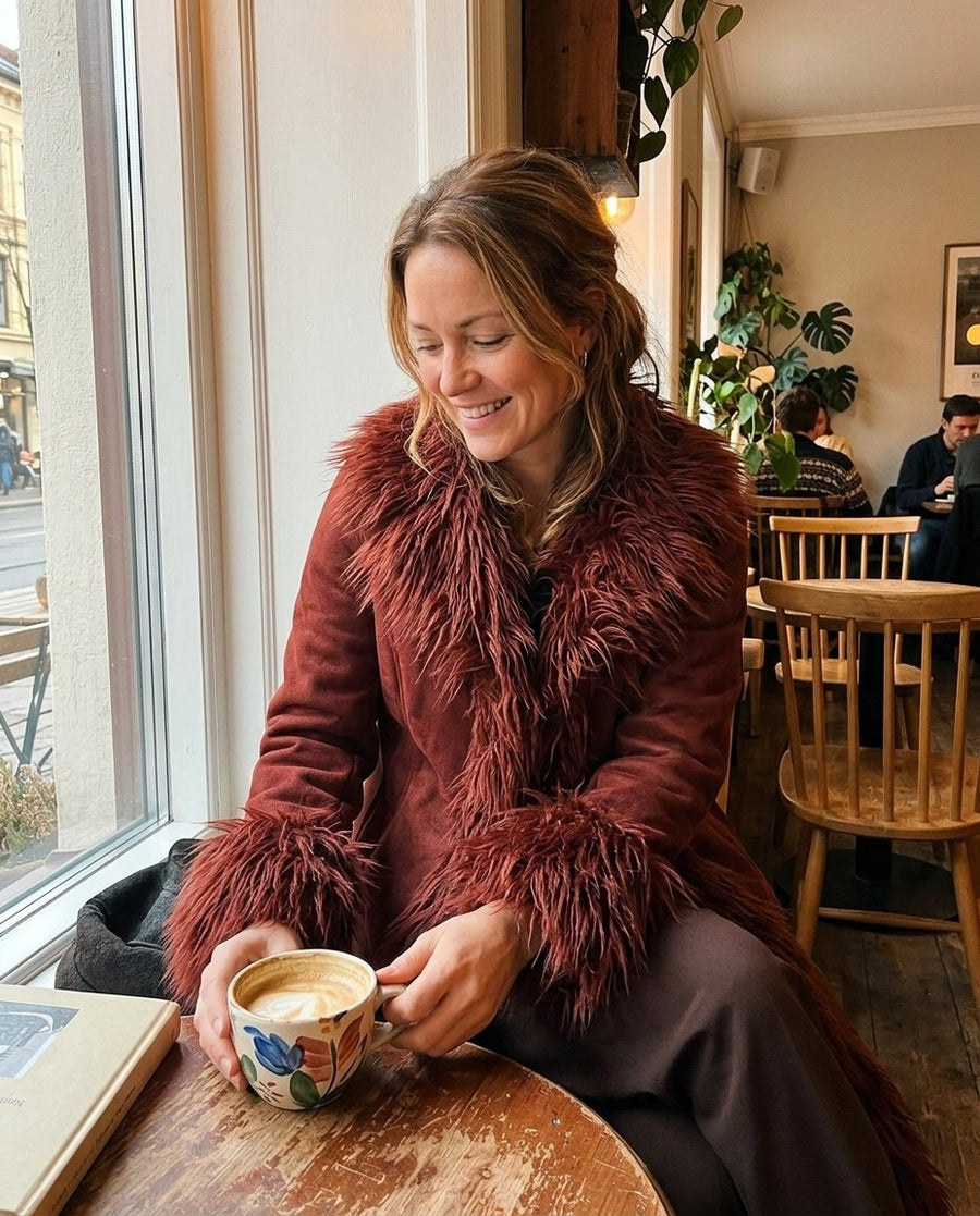 Lova, lång kappa i mockaimitation med fuskpälskant för dam i rödbrun, stylinginspiration på ett kafé