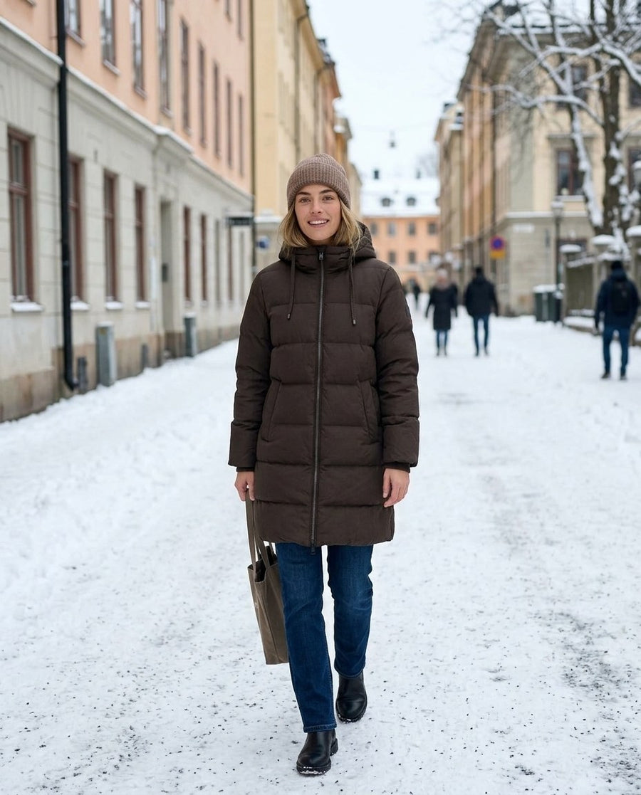 Tyra, lång vadderad jacka med huva för dam i brun, stylinginspiration på en snöig gata