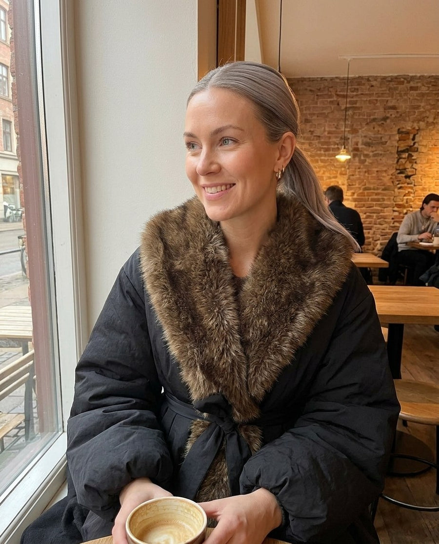 Tilda, vadderad damjacka med fuskpälskrage och skärp i svart, stylinginspiration på ett kafé