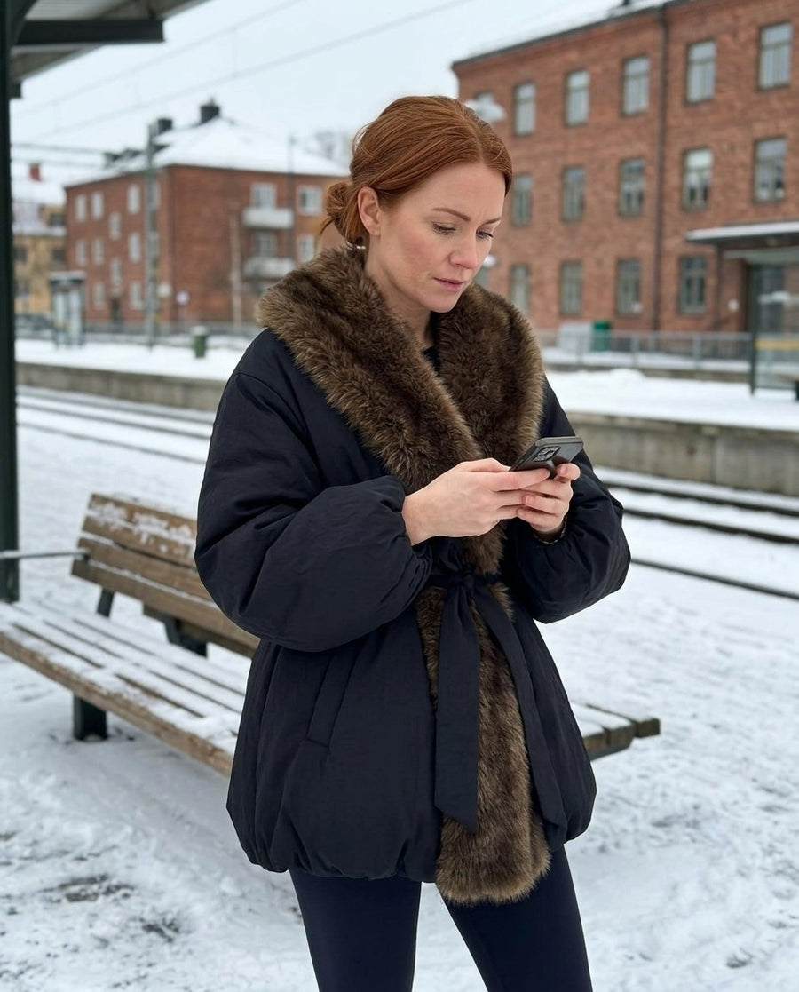 Tilda, vadderad damjacka med fuskpälskrage och skärp i svart, stylinginspiration på en perron