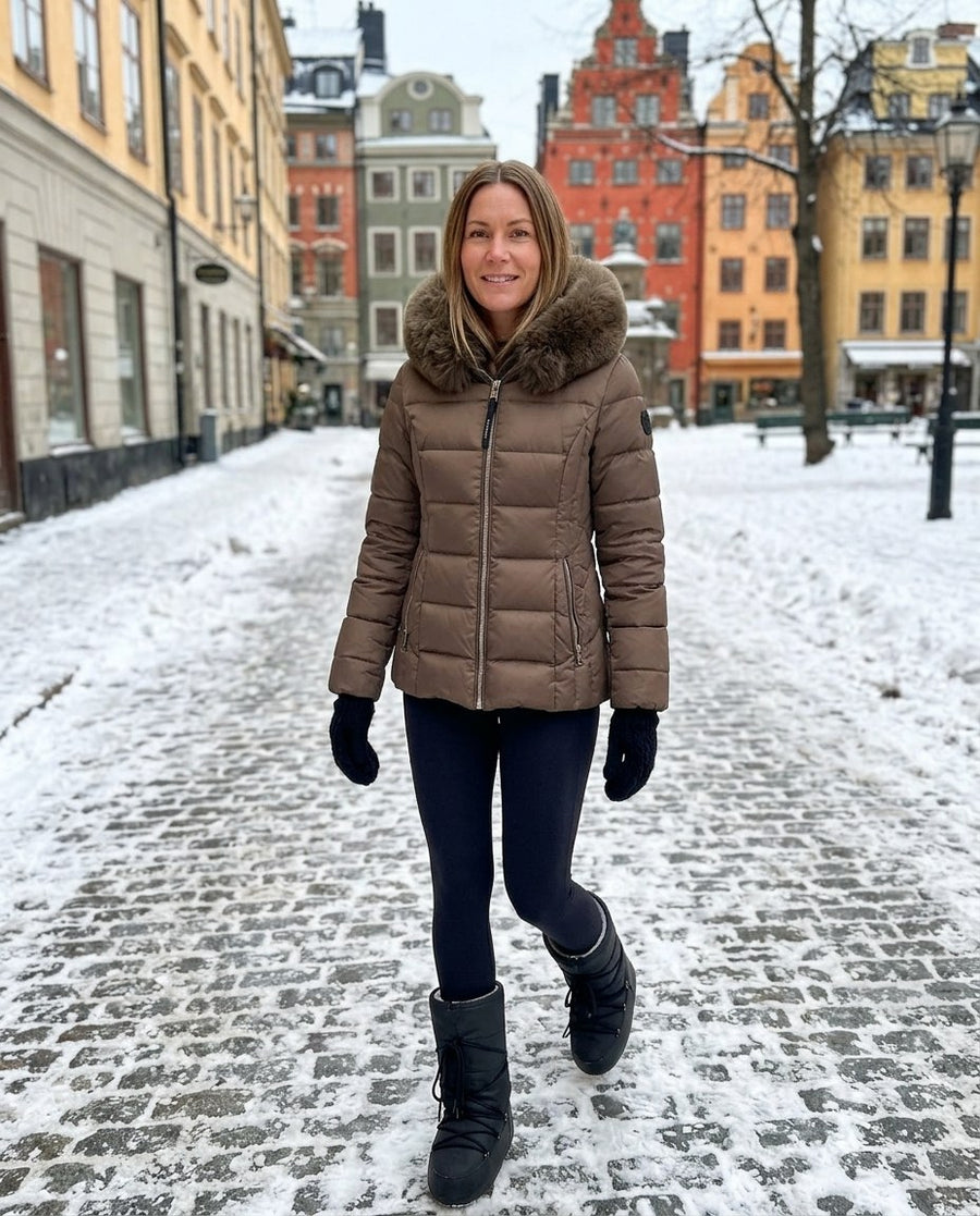 Wilma, vadderad jacka med fuskpälshuva för dam i brun, stylinginspiration på en snöig gata